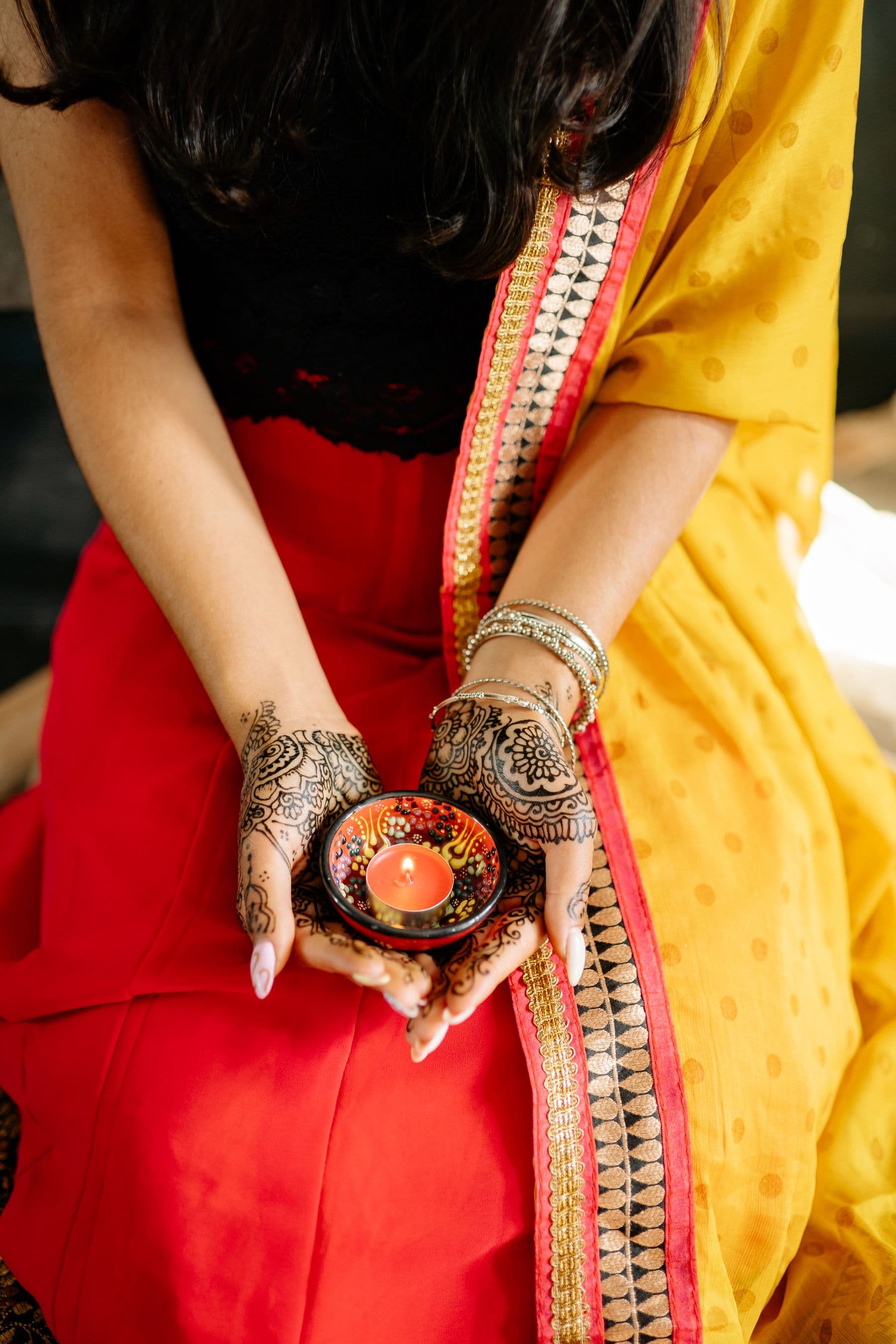 Henna-adorned hands carrying a lit diya